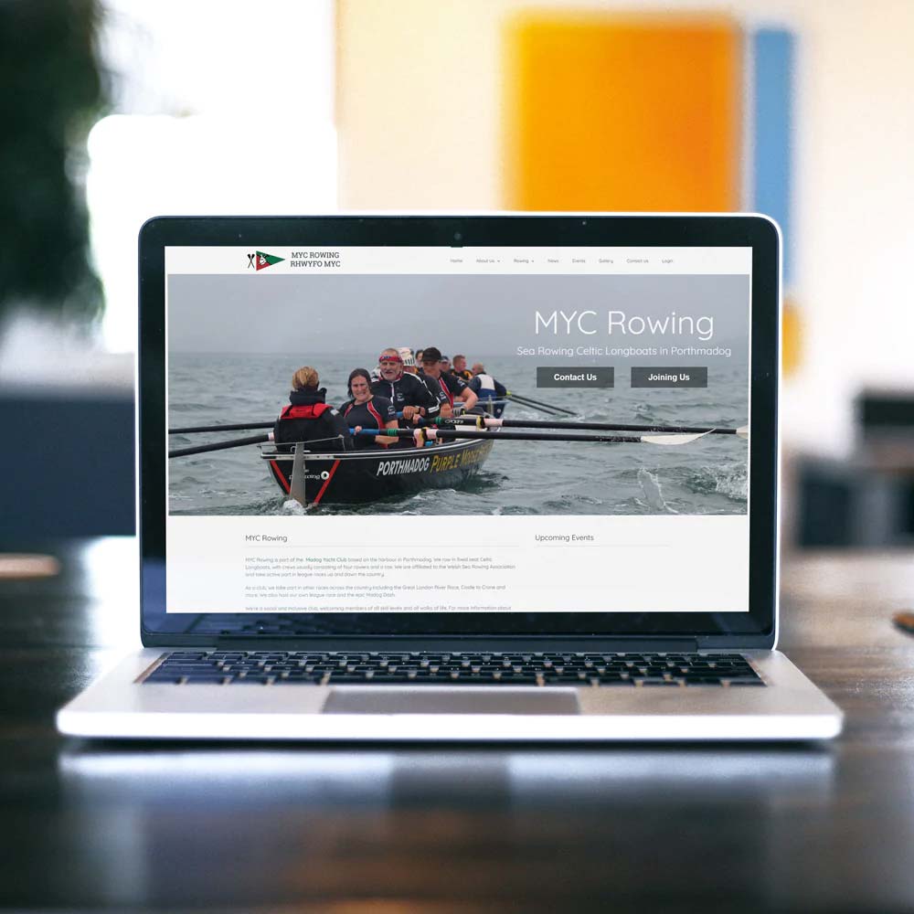 Lifestyle image of a laptop on desk showing the myc porthmadog rowing clubs website on the screen